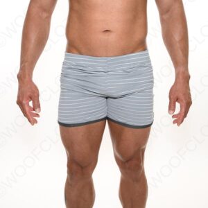 A fit male model freeballing in gray striped boxer briefs, showing his toned abdomen and muscular thighs against a plain white background.