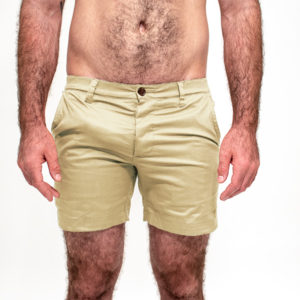 A guy wearing WOOF Commando Safe Chino Men's Short Shorts stands with his hands by his side, showing off hairy legs on a white background, and appears to be freeballing.