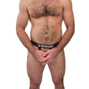 A guy with a hairy chest and legs, wearing WOOF Commando Safe Jockstrap (2nd Generation Generation, Black) with bulge enhancement, standing against a white background.